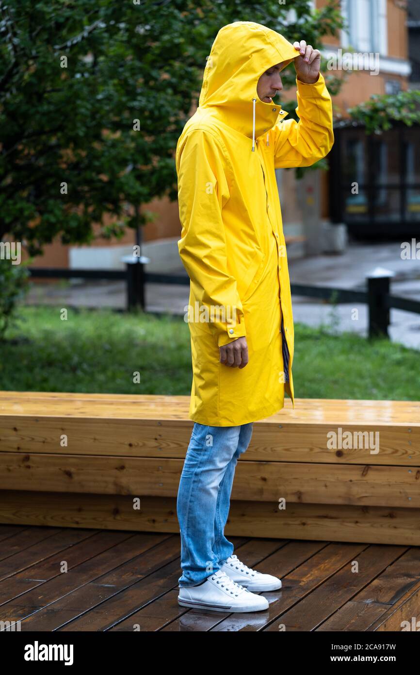 Homme en imperméable jaune avec la capuche debout sur un sol en bois humide  par temps pluvieux, vue latérale. Extérieur Photo Stock - Alamy