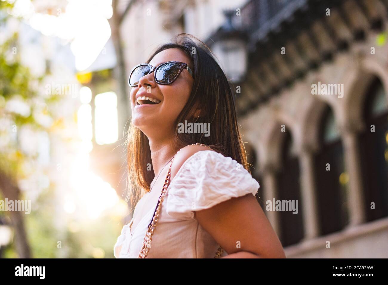 une femme avec des lunettes de soleil sourit lorsqu'elle se promène dans la ville Banque D'Images