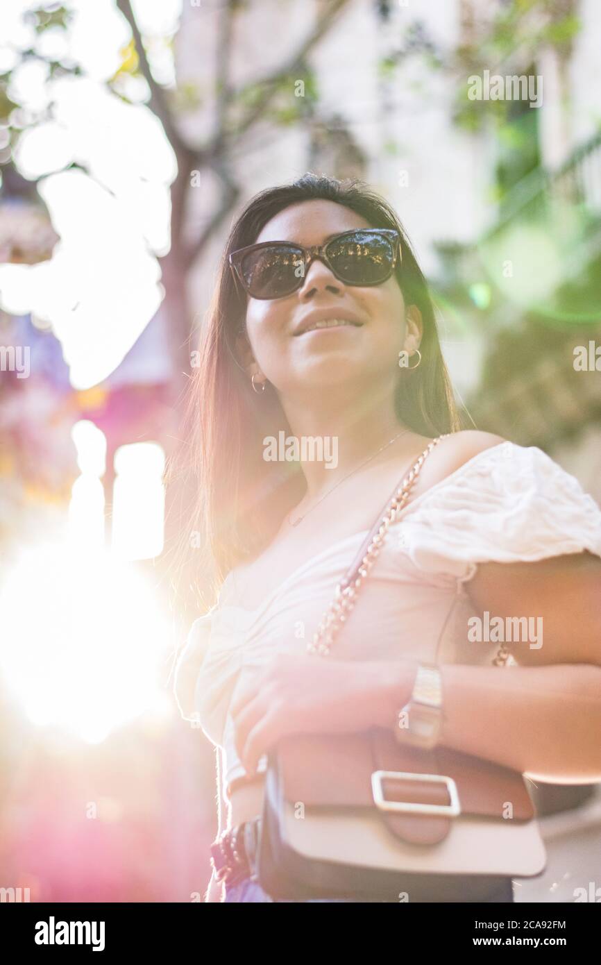une femme avec des lunettes de soleil sourit lorsqu'elle se promène dans la ville Banque D'Images