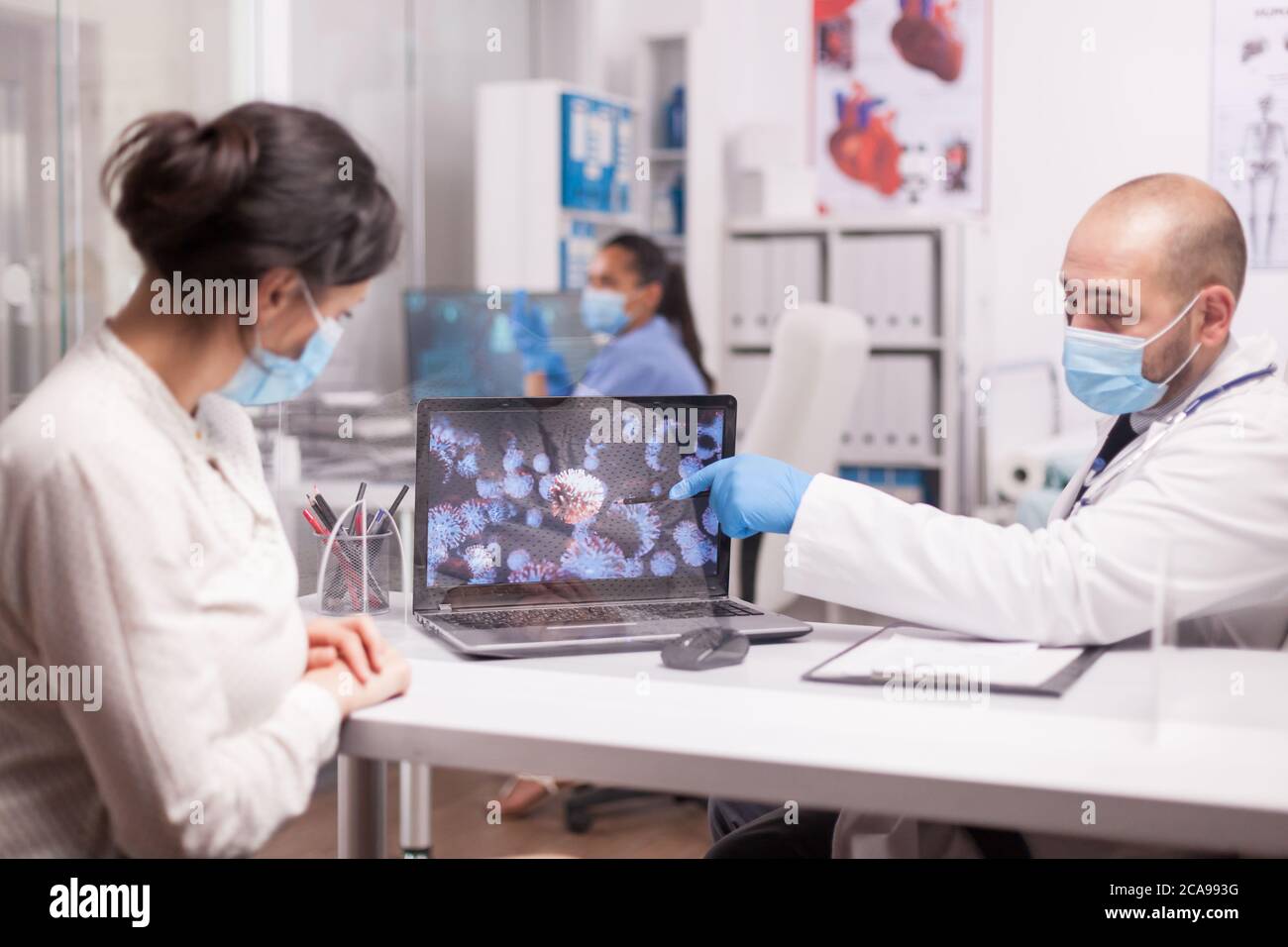 Médecin avec masque de protection pointant vers l'animation du coronavirus pendant la consultation du patient. Banque D'Images Médecin avec masque de protection pointant vers l'animation du coronavirus pendant la consultation du patient. Banque D'Images