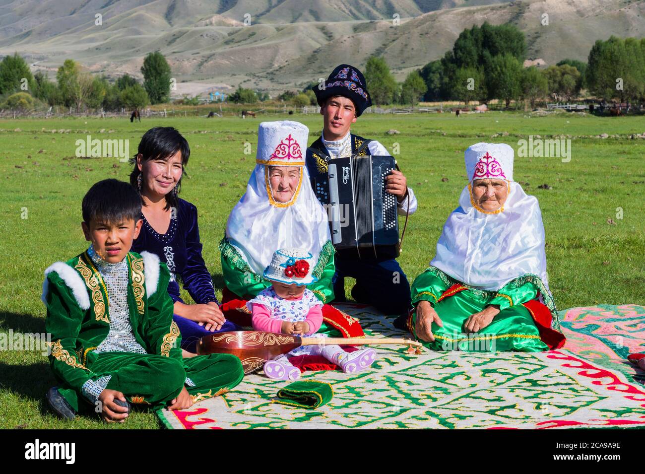 La famille kazakhe en vêtements traditionnels à écouter la musique d'un joueur d'accordéon, pour un usage éditorial uniquement, le sati village, Tian Shan, de Kazakhs Banque D'Images