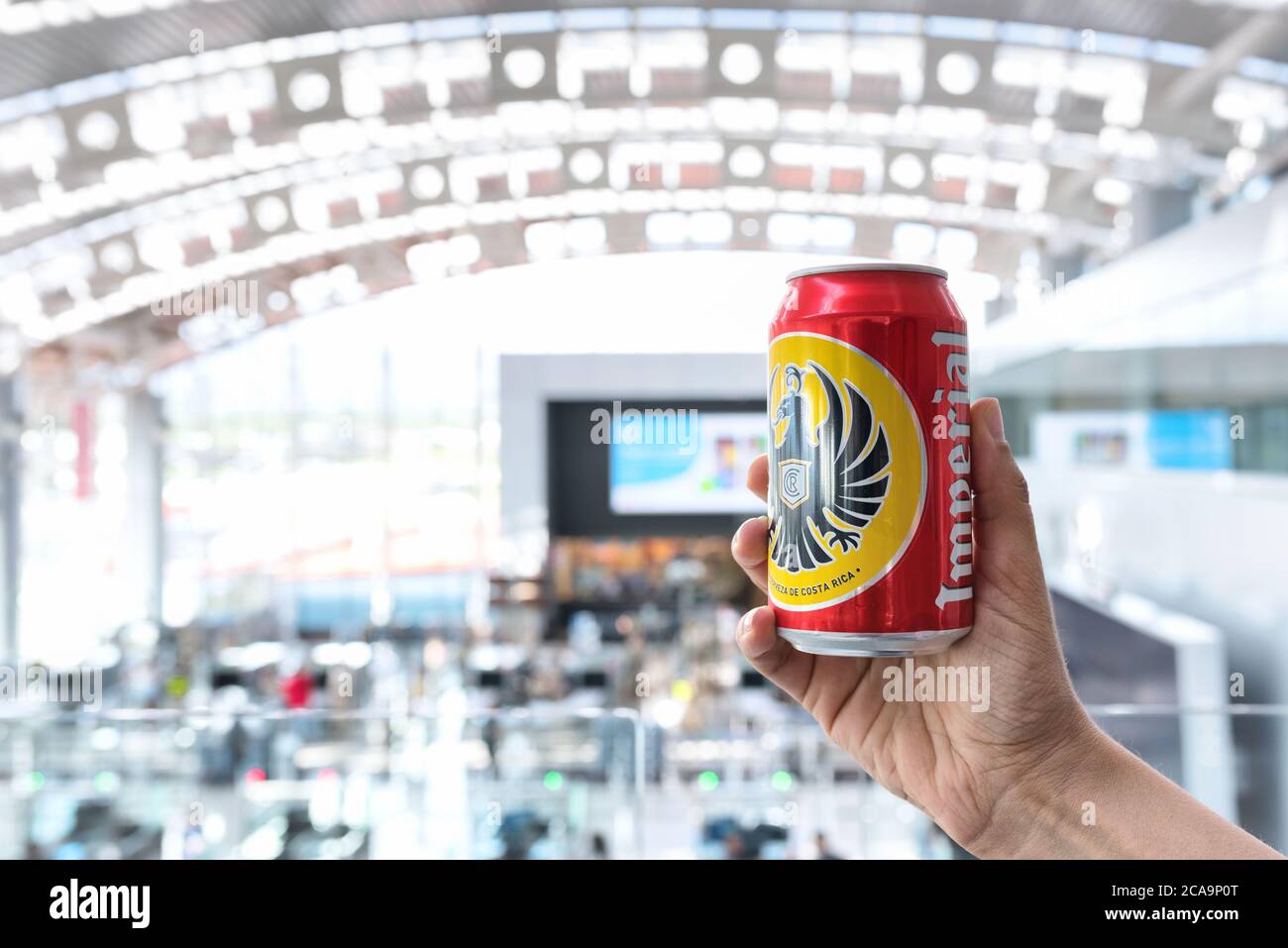 Main tenant une bière impériale peut, la marque de bière la plus commune du Costa Rica. Vue intérieure défocace de l'aéroport international Juan Santamaría. Banque D'Images Main tenant une bière impériale peut, la marque de bière la plus commune du Costa Rica. Vue intérieure défocace de l'aéroport international Juan Santamaría. Banque D'Images