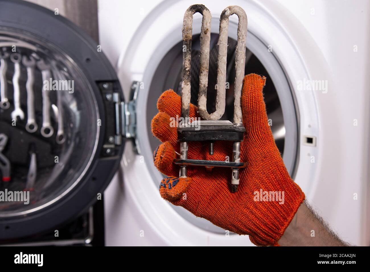 Réparation de machines à laver. Main d'un réparateur avec un chauffage électrique turbulent recouvert d'un revêtement d'eau dure. Remplacement du chauffage électrique Banque D'Images