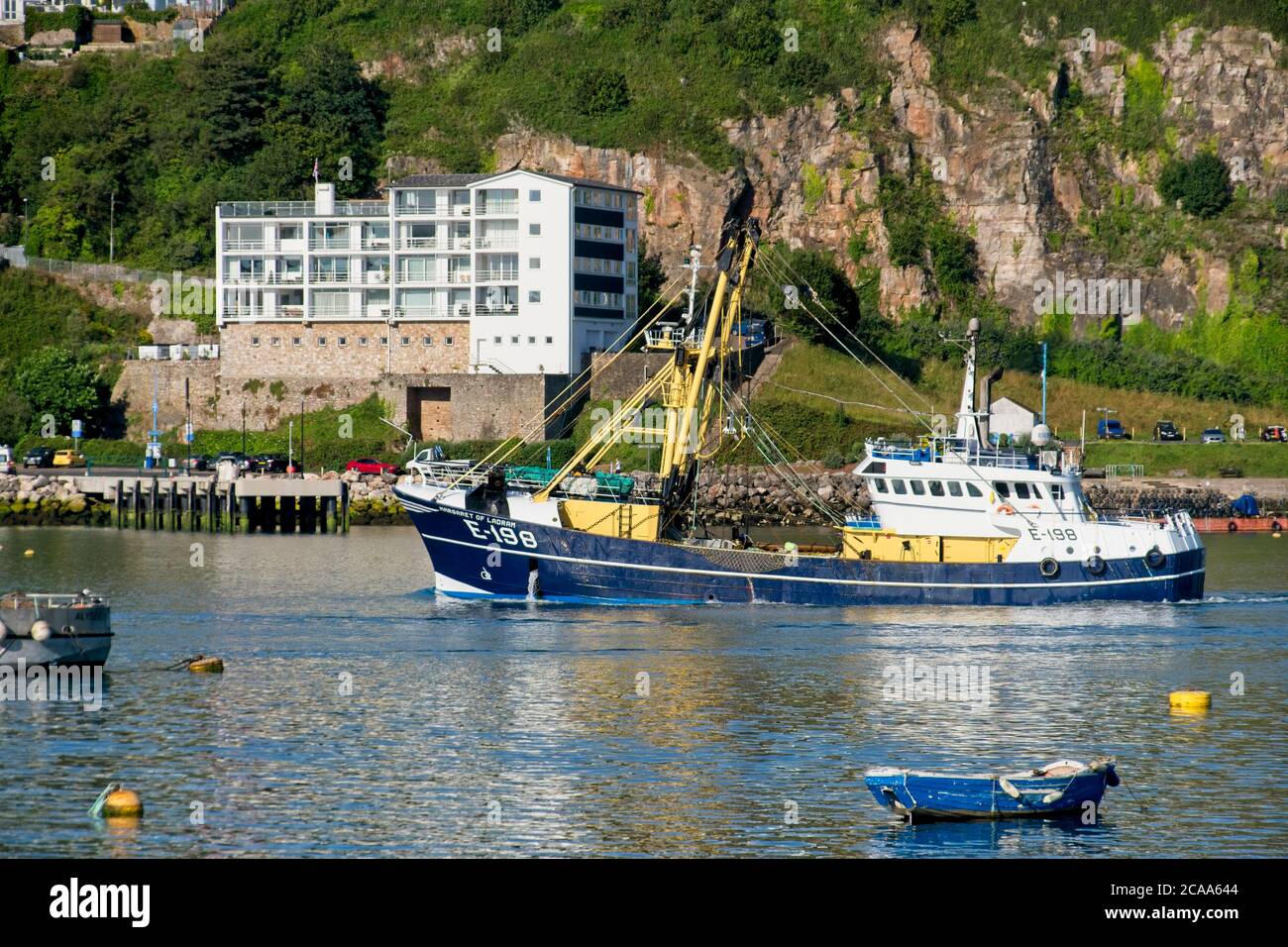 Brixham Trawler E198 MARGARET DE LAPDRAM retournant au port. Chalutiers dans le port de Brixham. Grand bâtiment et falaises en arrière-plan. Format paysage Banque D'Images
