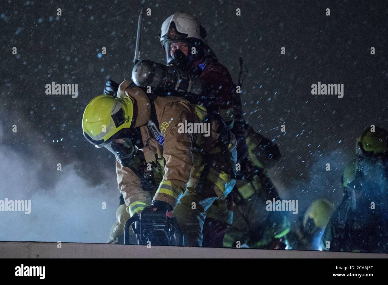 Les pompiers utilisant une hache et une scie sur le toit impliqué en cas d'incendie Banque D'Images