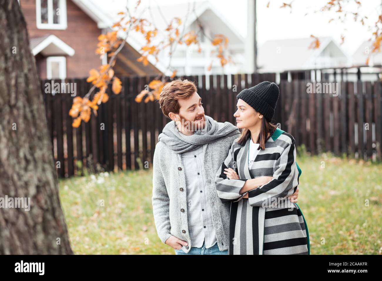 Joyeux jeune couple assis à l'extérieur, devant leur nouvelle maison en automne vêtements chauds et rêvant de leur nouvel achat passionnant. Banque D'Images