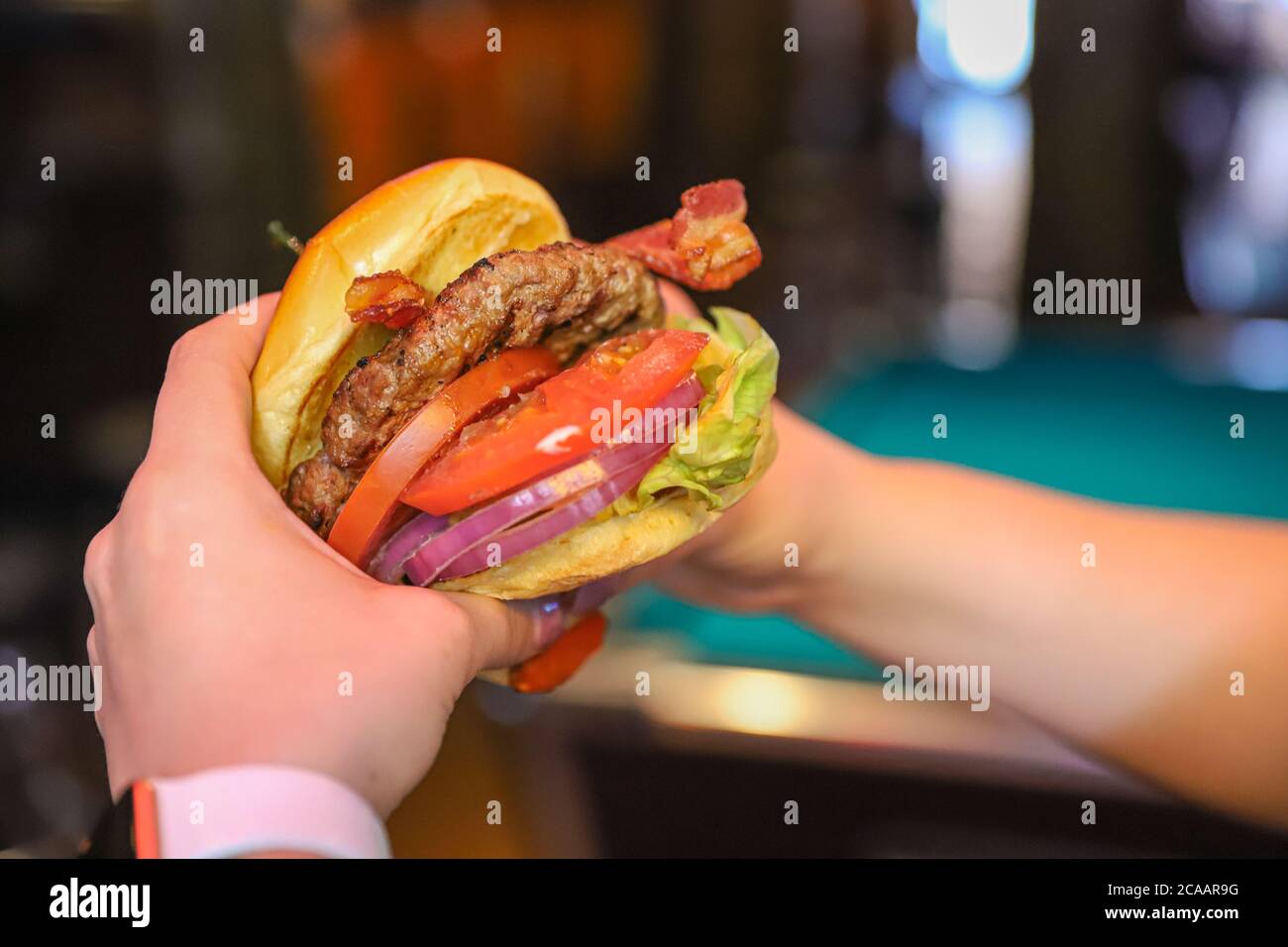 LONG BEACH, CALIFORNIE, ÉTATS-UNIS - 13 janvier 2020 : les mains d'une femme tiennent un hamburger dans un bar-restaurant faiblement éclairé. Banque D'Images