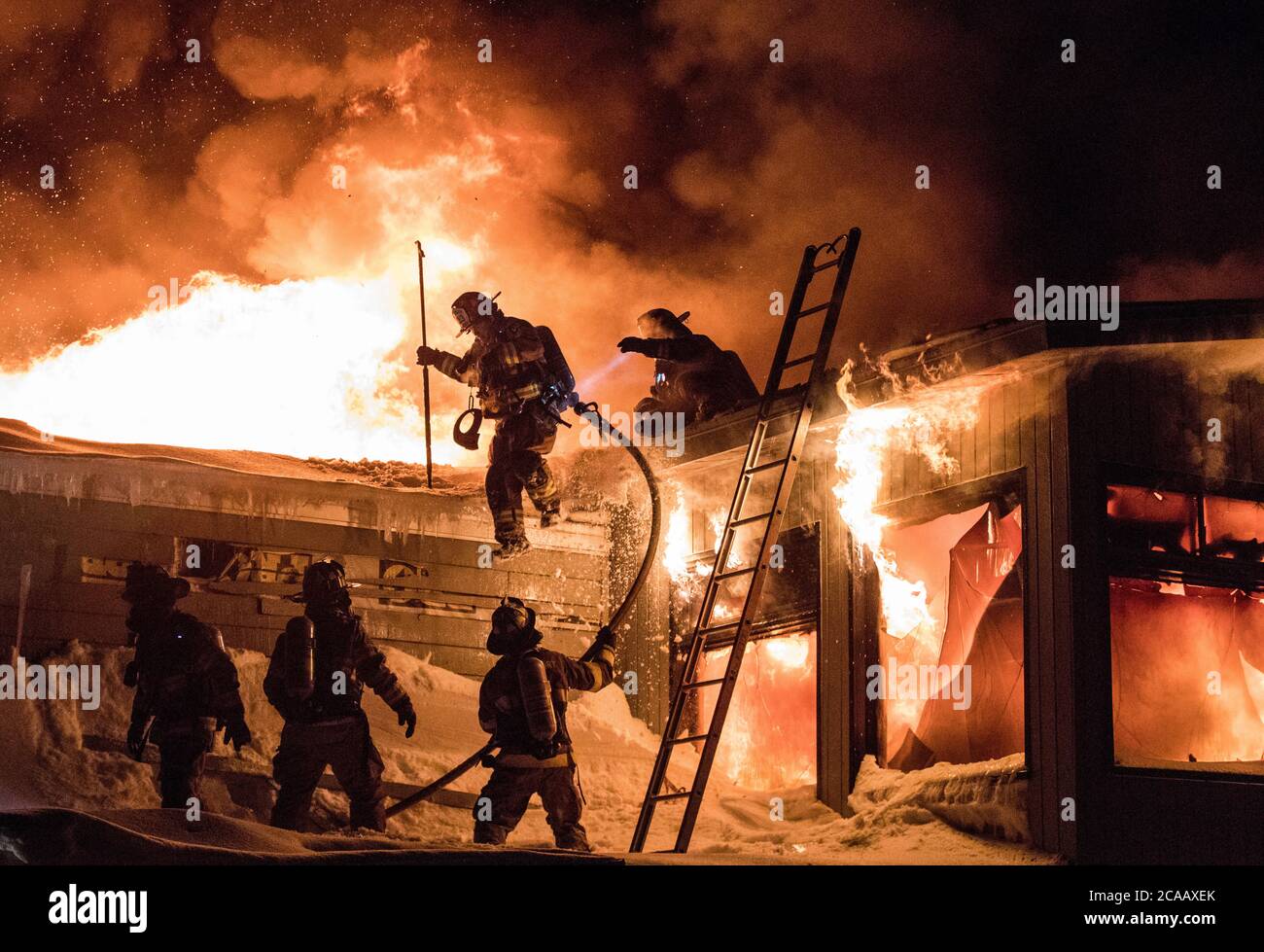 Un incendie énorme dans un bâtiment commercial et un pompier sur un toit en conditions hivernales. Banque D'Images