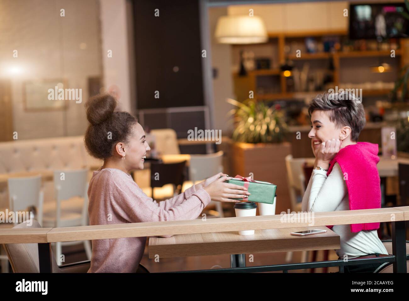 Happy woman félicite son amie à présent fort tout en restant assis dans un café du centre commercial. L'amitié féminine, des amies, des vacances celebratin Banque D'Images
