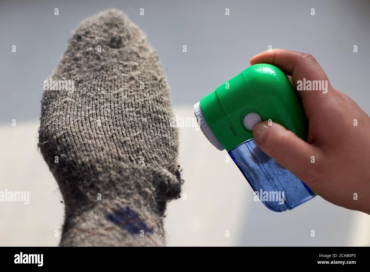 Femme enlève les peluches des chaussettes de laine avec l'aide d'une machine électrique, gros plan. Banque D'Images