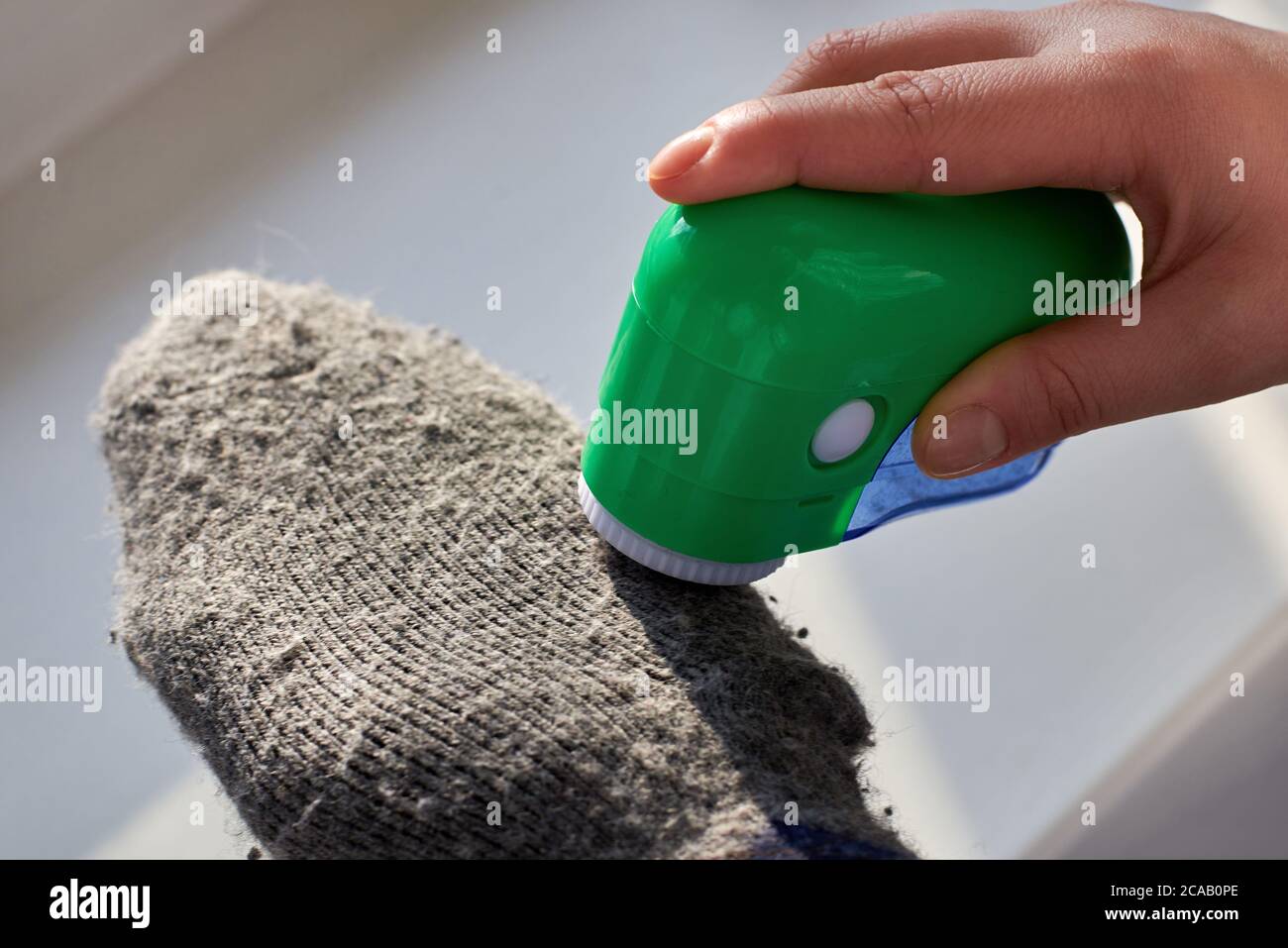 Femme enlève les peluches des chaussettes de laine avec l'aide d'une machine électrique, gros plan. Banque D'Images
