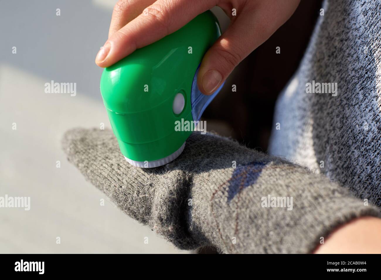 Femme enlève les peluches des chaussettes de laine avec l'aide d'une machine électrique, gros plan. Banque D'Images