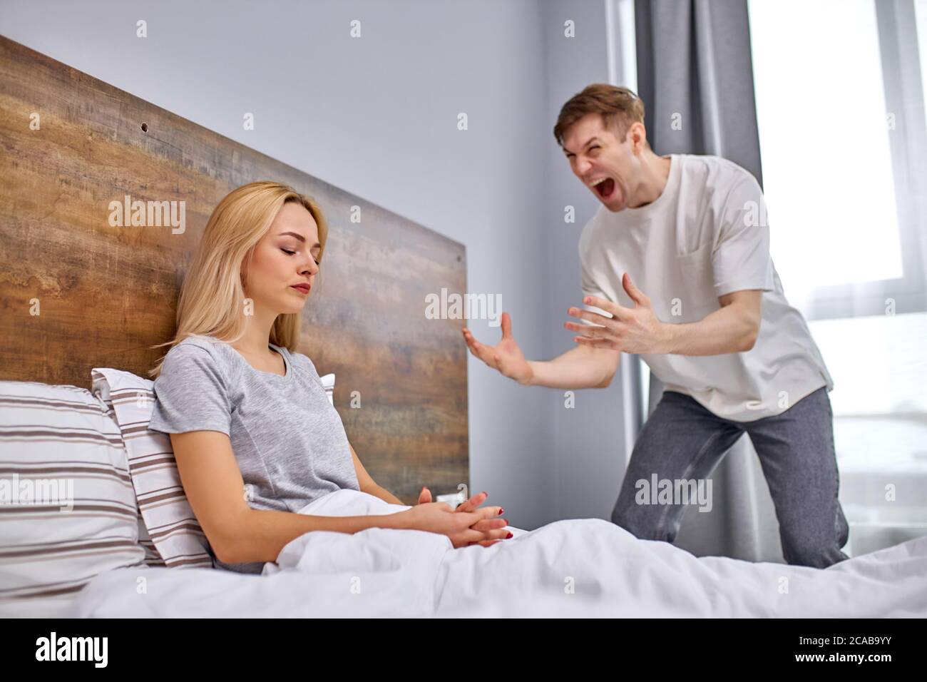 le mari hystérique exprime le mécontentement, la femme ne s'en soucie pas, s'asseoir sur le lit n'ayant aucune émotion, elle est émotionnellement dévastée Banque D'Images