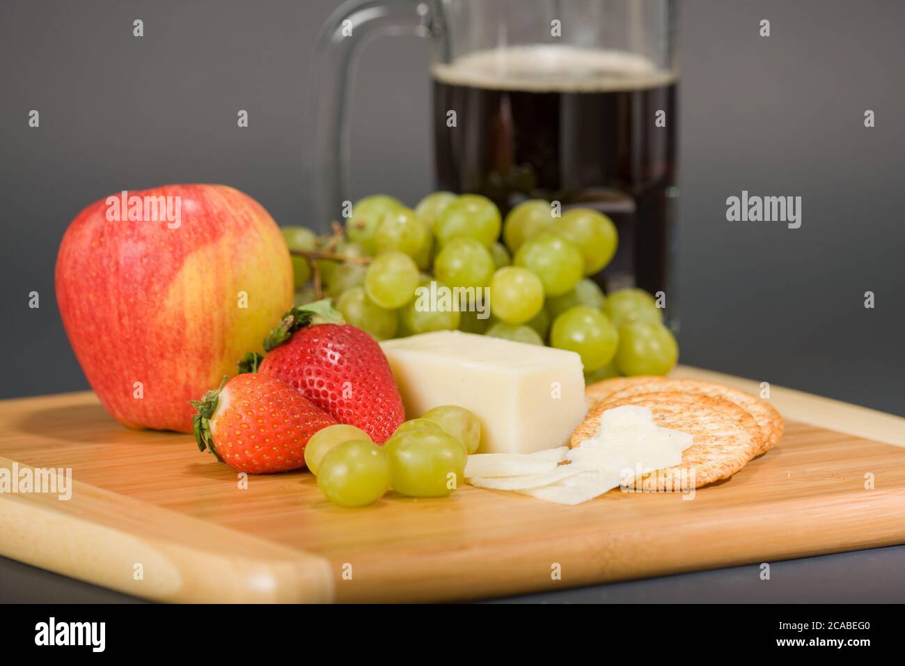 Gruyere fromage suisse, tasse de bière, fruits et crackers de blé entier sur une planche à découper en bois Banque D'Images