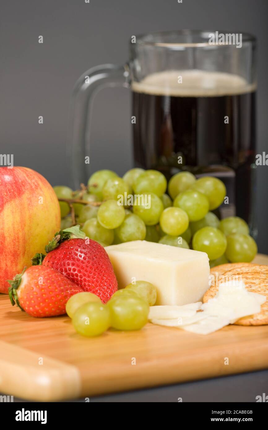 Gruyere fromage suisse, tasse de bière, fruits et crackers de blé entier sur une planche à découper en bois Banque D'Images