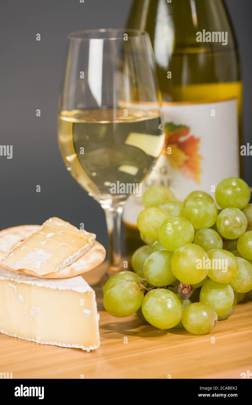 Brie bébé fumé, raisins, crackers d'eau, verre et bouteille de vin de Chardonnay sur la planche à découper Banque D'Images