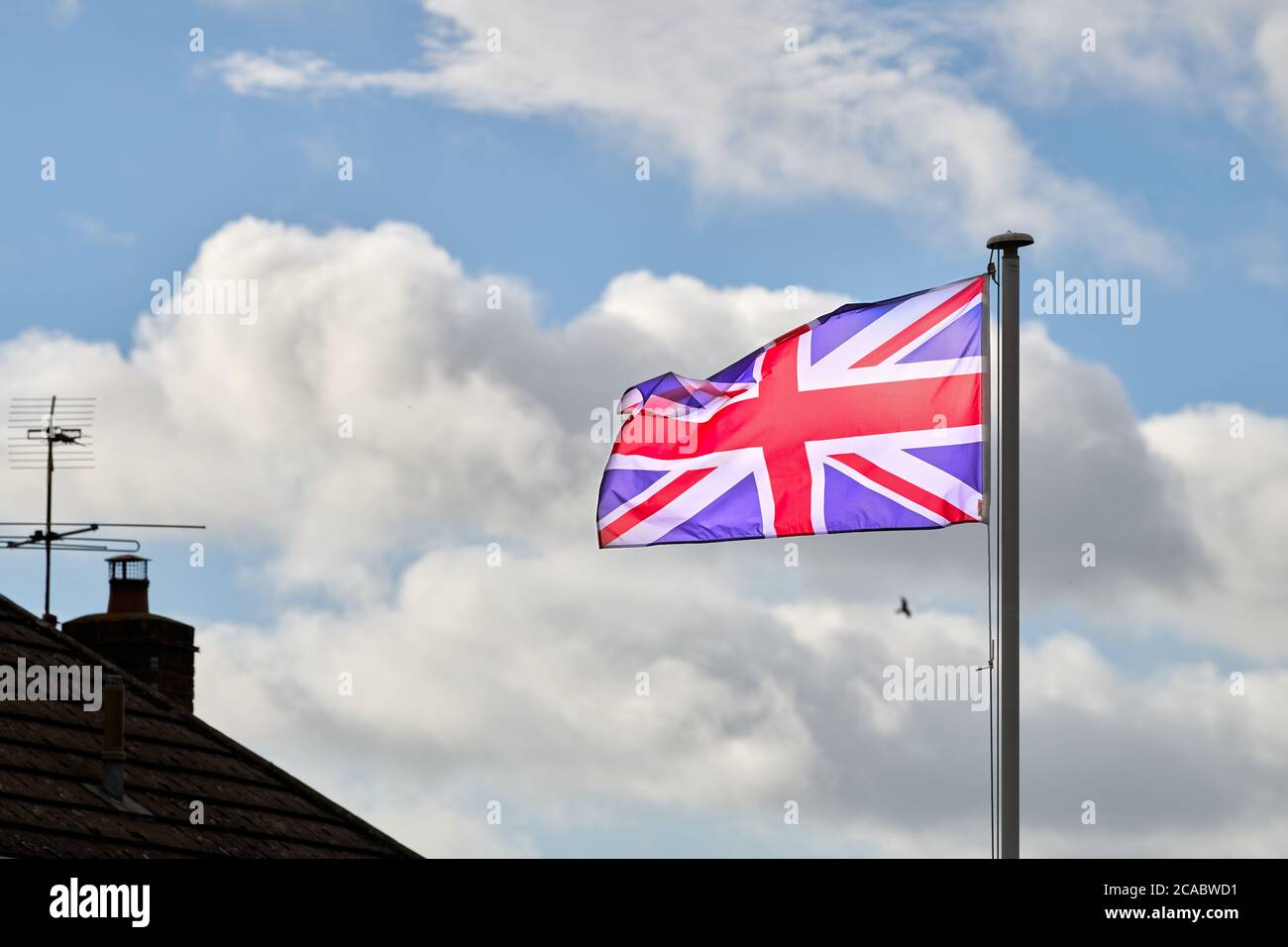 Drapeau Union Jack, symbole du Royaume-Uni d'Angleterre et du pays de Galles, de l'Écosse et de l'Irlande du Nord, flotte dans le vent, abdevant le toit d'une maison. Banque D'Images