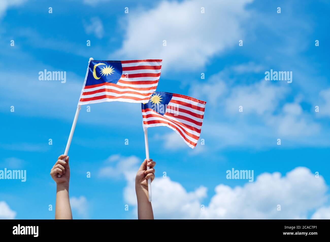 Main joyeuse agitant le drapeau de la Malaisie contre le ciel bleu. Fêtez l'indépendance et la Merdeka. Banque D'Images