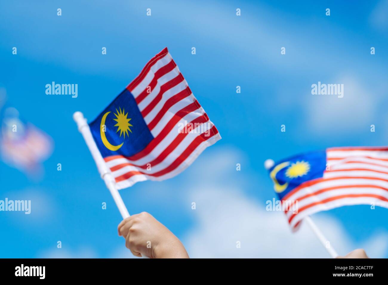 Main joyeuse agitant le drapeau de la Malaisie contre le ciel bleu. Fêtez l'indépendance et la Merdeka. Banque D'Images
