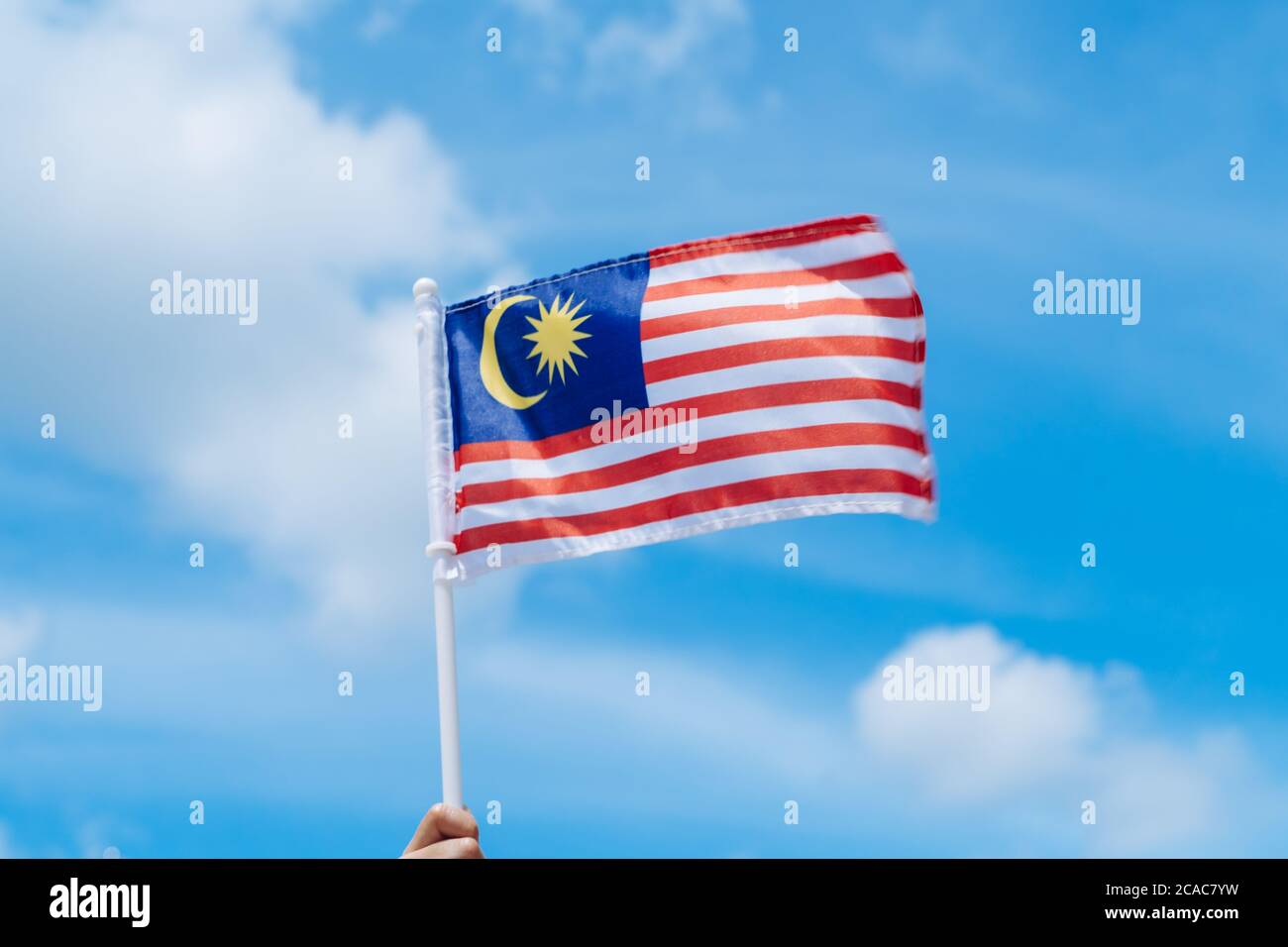 Main joyeuse agitant le drapeau de la Malaisie contre le ciel bleu. Fêtez l'indépendance et la Merdeka. Banque D'Images