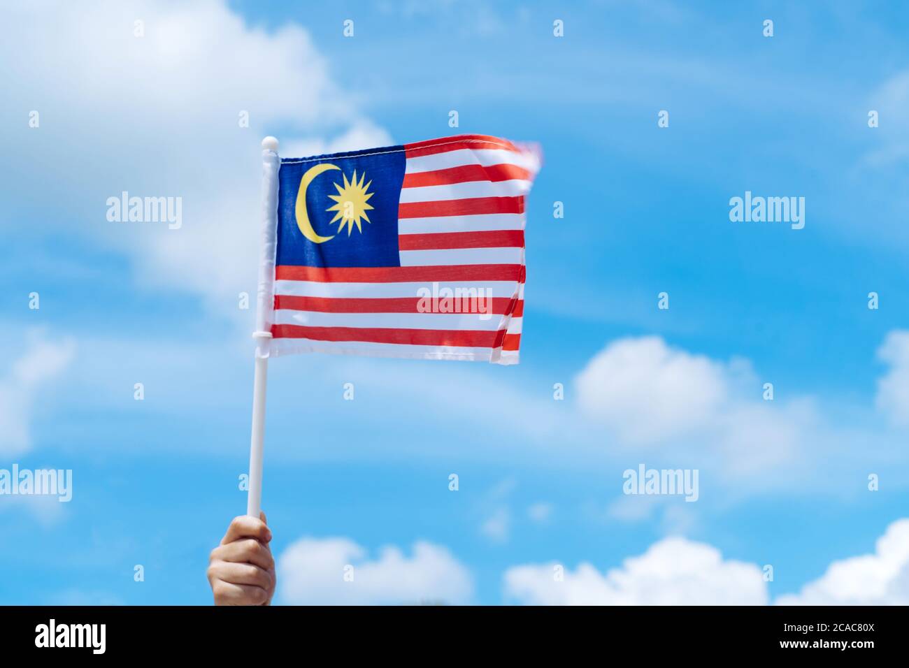 Main joyeuse agitant le drapeau de la Malaisie contre le ciel bleu. Fêtez l'indépendance et la Merdeka. Banque D'Images
