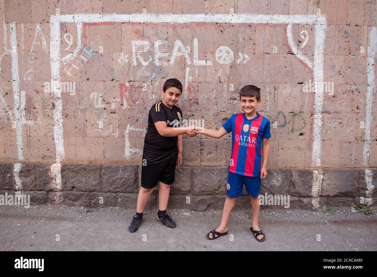 Alaverdi / Arménie - 20 juillet 2019: Amis enfants avec des chemises des équipes rivales Real Madrid et FC Barcelone posant devant le but de football peint sur le mur Banque D'Images