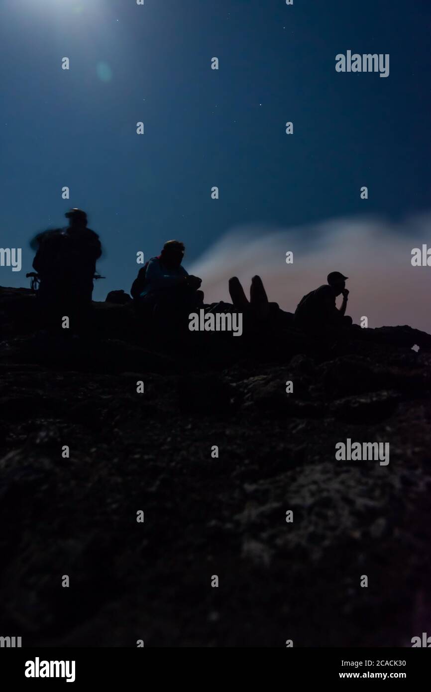 Silhouettes de personnes assises au bord du cratère du volcan Erta Ale, en Éthiopie, en pleine lune Banque D'Images