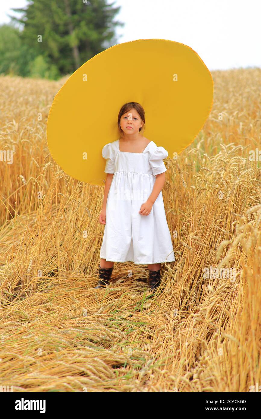 Enfant dans un énorme chapeau jaune dans un champ de blé en été Banque D'Images
