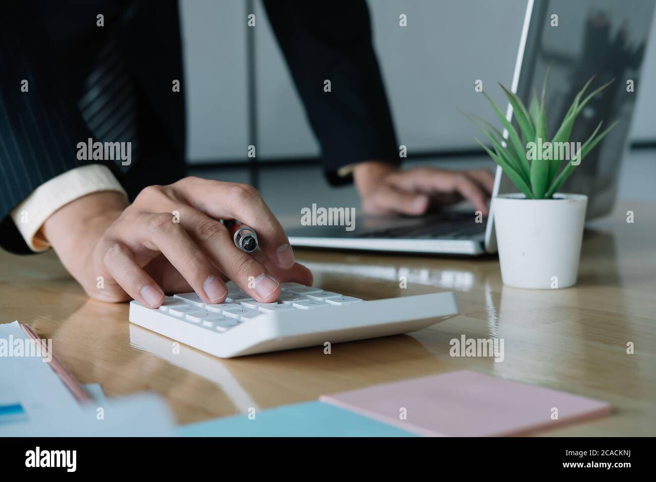 Gros plan d'un homme d'affaires ou d'un comptable tenant un stylo travaillant sur la calculatrice pour calculer les données d'entreprise, le document comptable et l'ordinateur portable à Banque D'Images