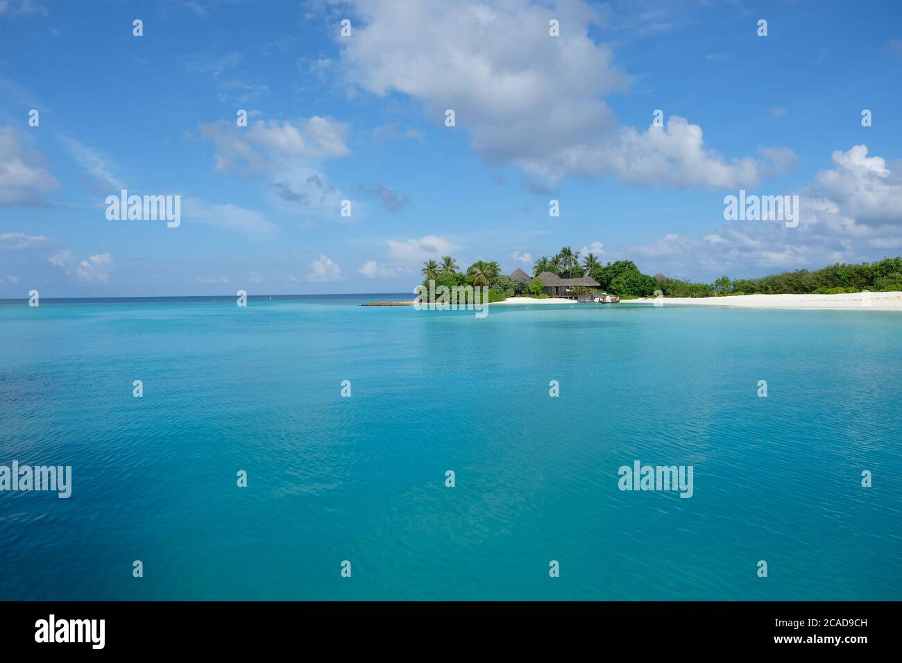 Petite île de la péninsule avec forêt verte et maisons. Large océan bleu dans la station de Maldive Island. Ciel bleu ciel nuageux ensoleillé Banque D'Images