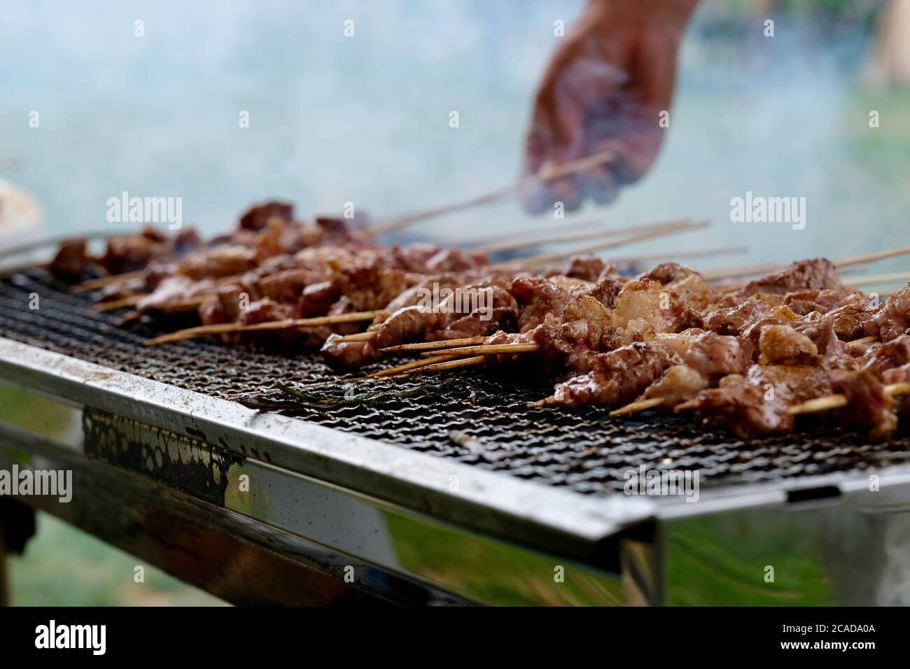 gros plan délicieux barbecue en bâtonnets de bambou sur le gril en métal. La fumée chaude monte. Une main est la cuisine. Concept de fête barbecue extérieur Banque D'Images