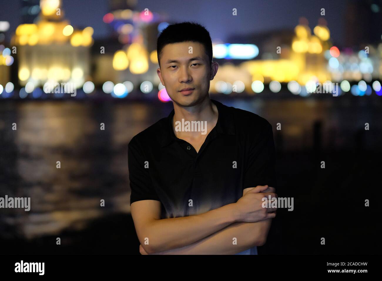 Un jeune asiatique debout au Bund à Shanghai la nuit. Arrière-plan des lumières de ville colorées et défocacées Banque D'Images