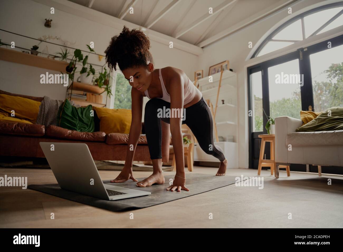 Bonne femme regardant la vidéo sur un ordinateur portable tout en s'exerçant sur un tapis de yoga à la maison - verrouillage de l'entraînement Banque D'Images