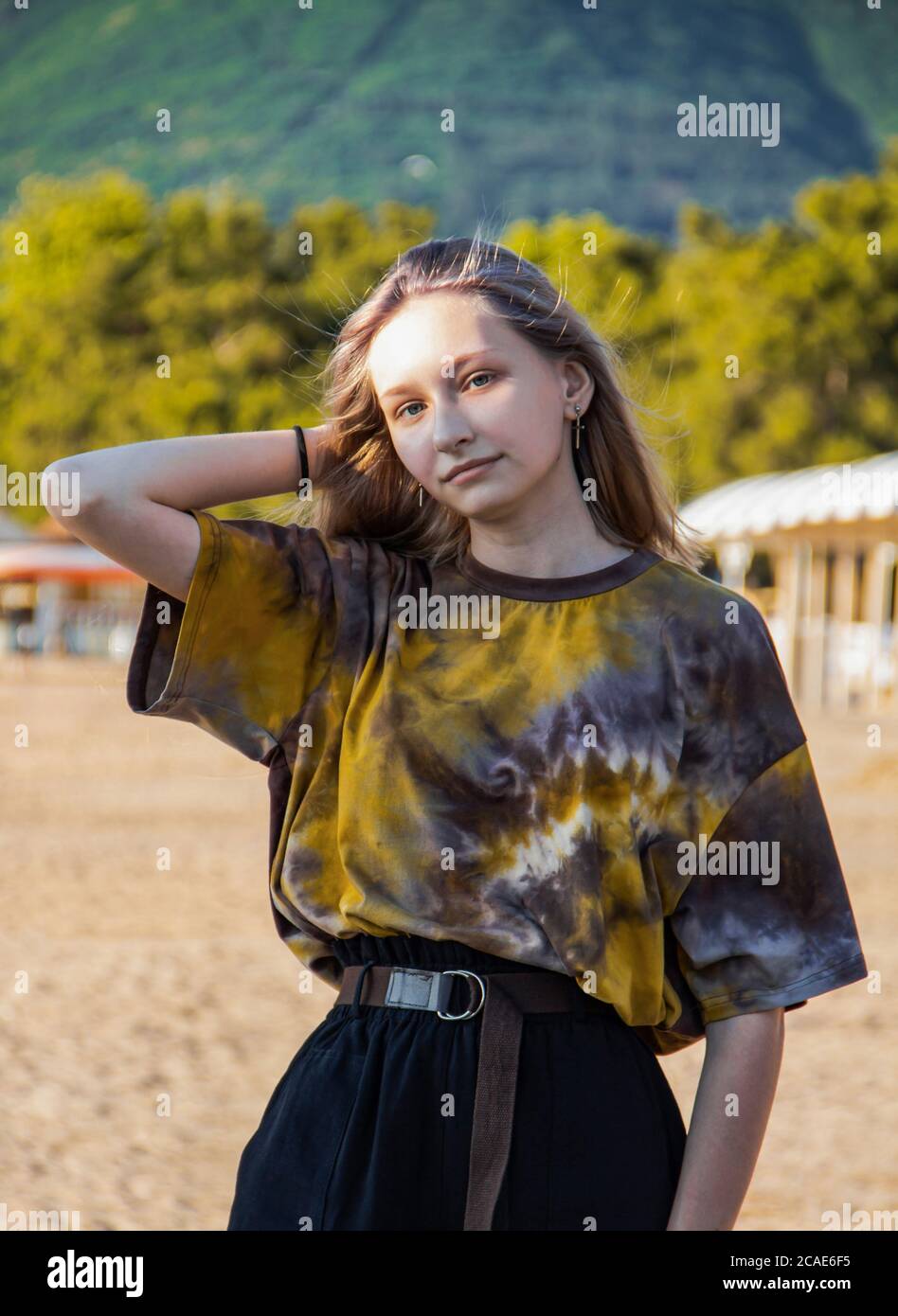 portrait d'une jolie jeune fille en vêtements à la mode, posé sur une plage de sable, sur fond d'arbres et de montagnes vertes. Banque D'Images