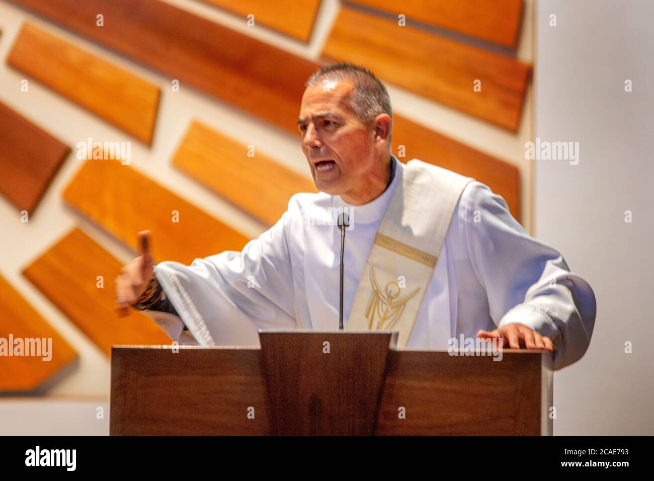 Portant une robe blanche, un diacre enthousiaste prêche un sermon dans la chaire d'une église catholique de Tustin, CA. Banque D'Images