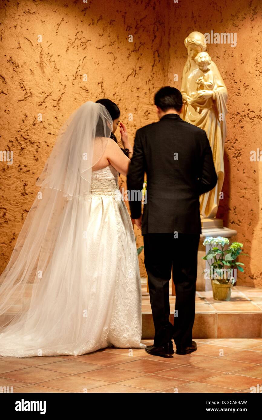 Une épouse et un époux juste mariés prient à la statue de la Vierge Marie et de l'enfant Christ dans une église catholique du sud de la Californie. Banque D'Images
