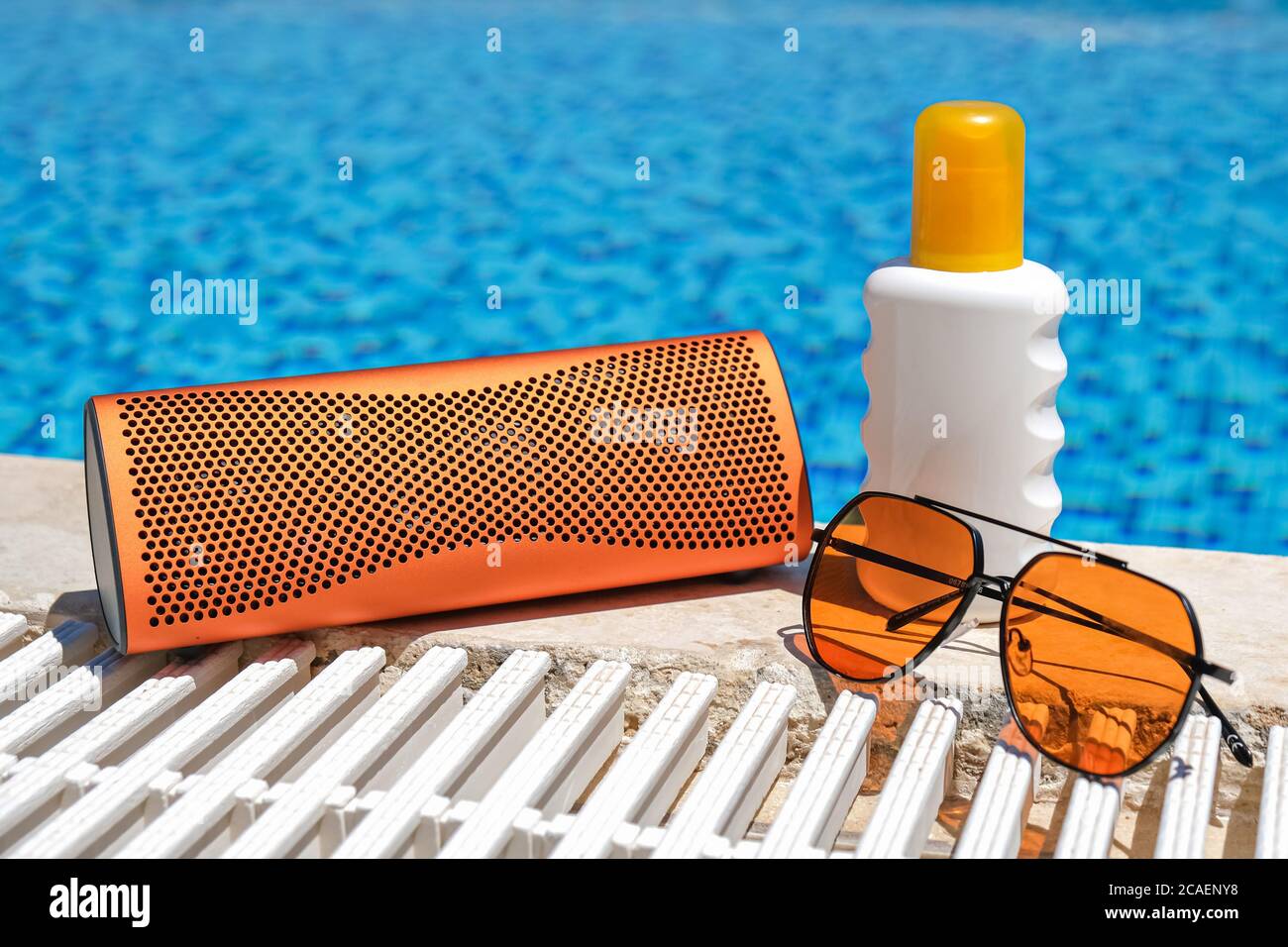accessoires de plage de couleur orange près de la piscine. Crème solaire,  lunettes de soleil, haut-parleur bluetooth de musique Photo Stock - Alamy