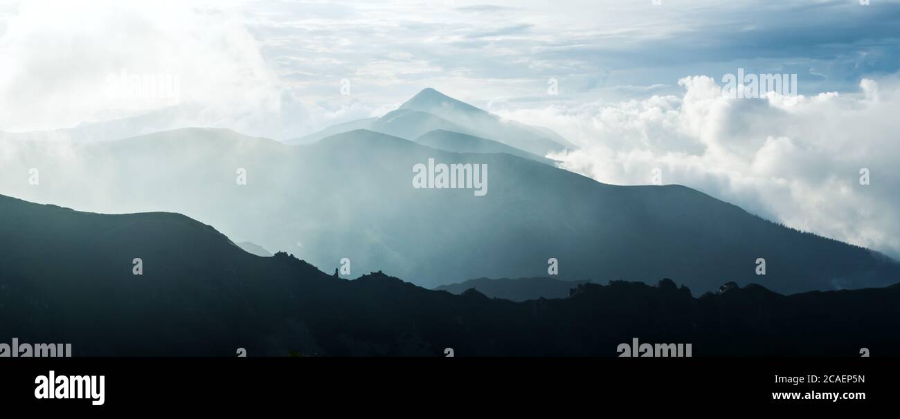 Panorama de beauté bleu de la gamme de montagnes brumeuses. Ciel nuageux et pics de montagne sombres avec brume lumineuse. Photographie de paysage Banque D'Images