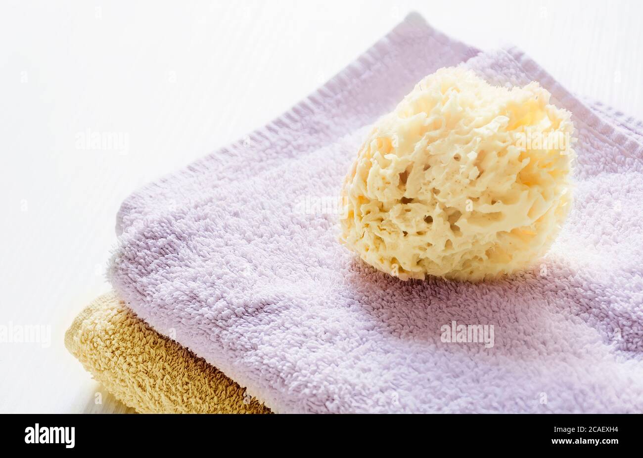 Une éponge jaune naturel sur les serviettes empilées sur une table en bois blanc. Soins personnels et hygiène. Bain et détente Banque D'Images