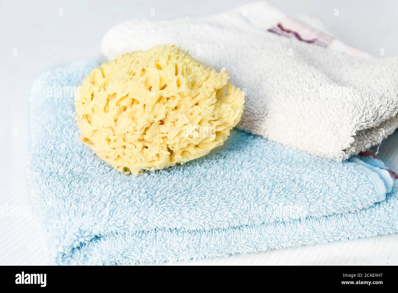 Une éponge jaune naturel sur les serviettes empilées sur une table en bois blanc. Soins personnels et hygiène. Bain et détente Banque D'Images