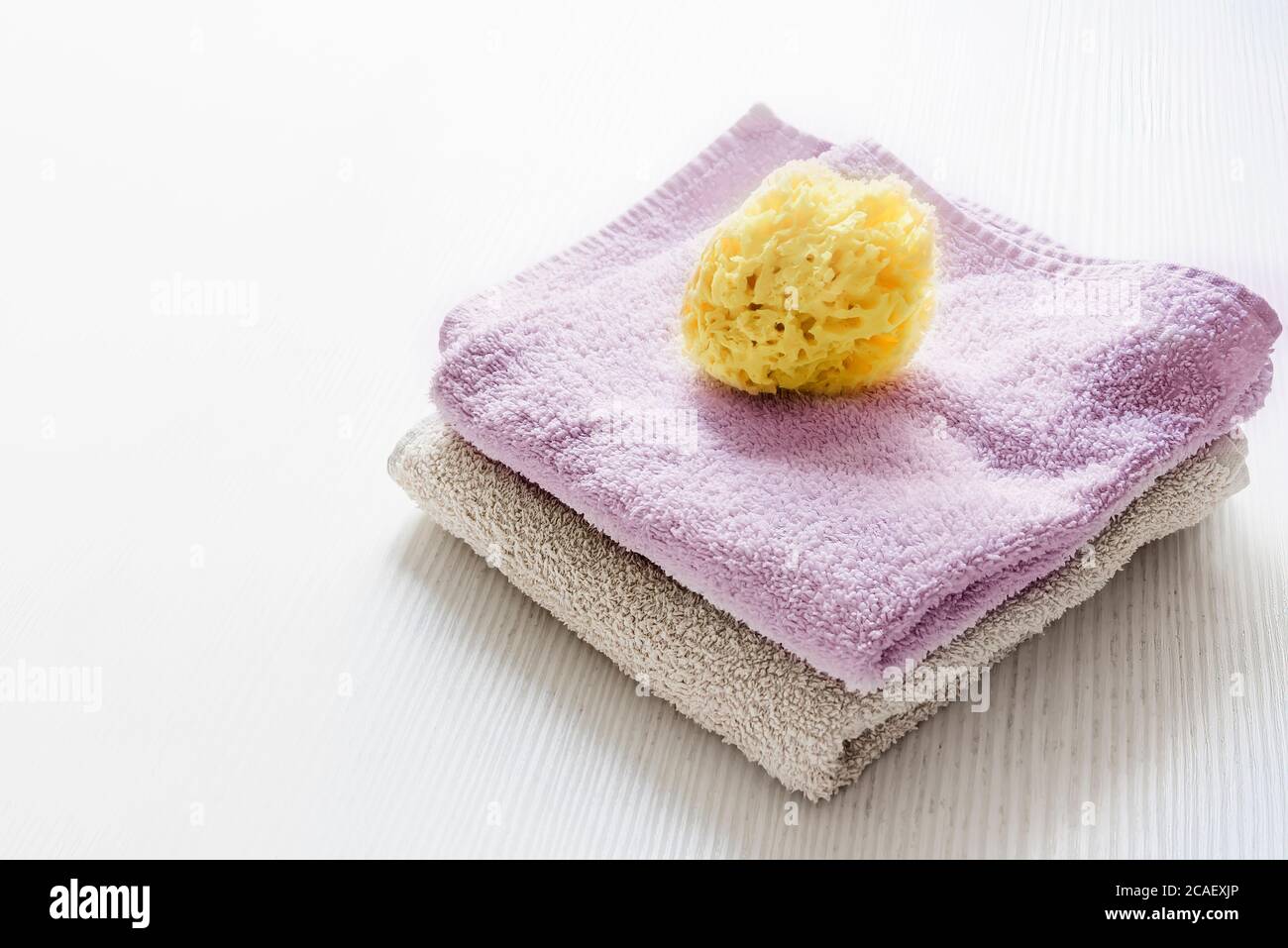 Une éponge jaune naturel sur les serviettes empilées sur une table en bois blanc. Soins personnels et hygiène. Bain et détente Banque D'Images