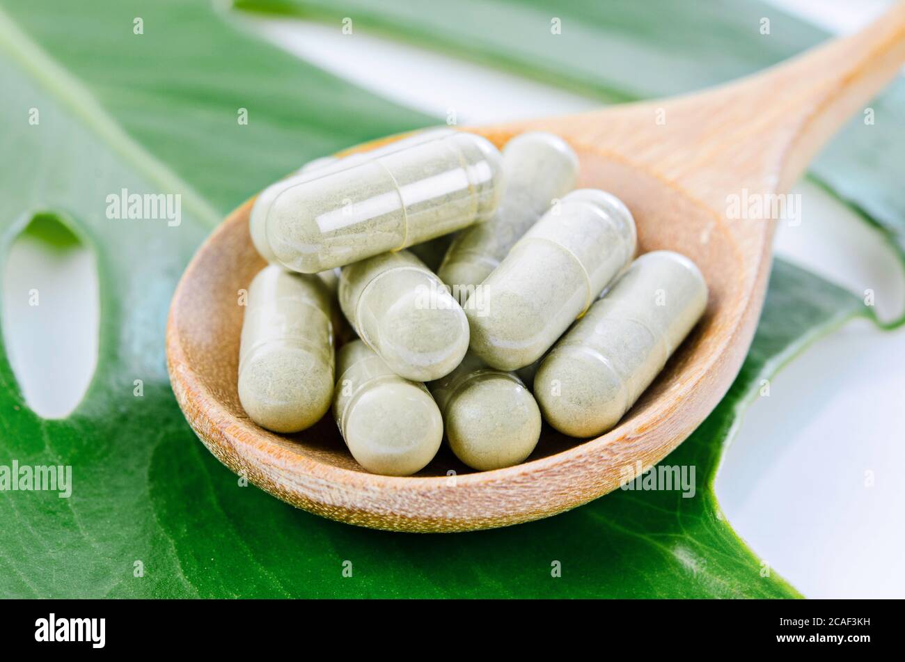 Capsules de médecine d'herbes dans une cuillère en bois avec une feuille verte. Banque D'Images