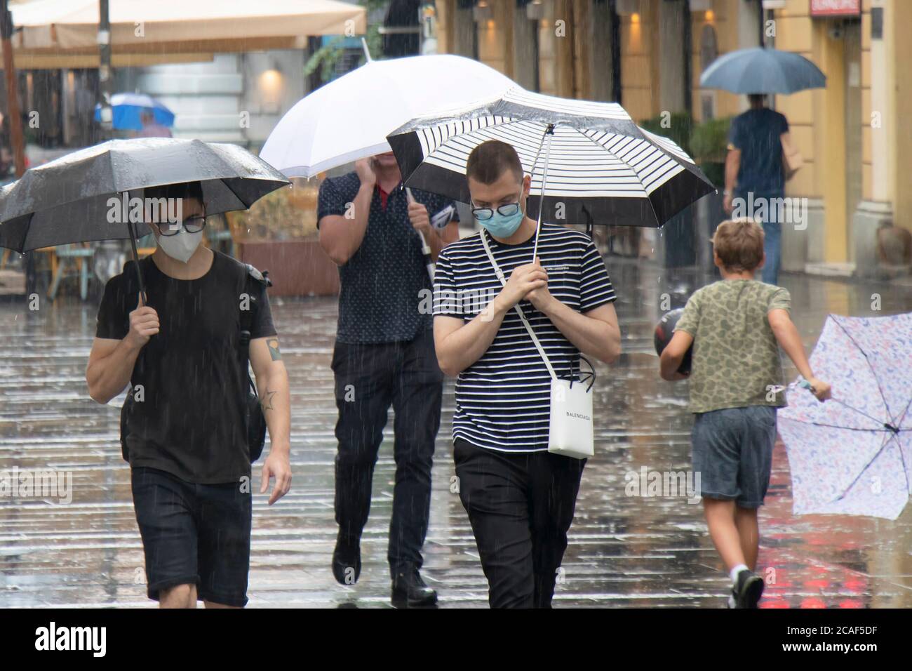 Belgrade, Serbie - 5 août 2020 : deux jeunes hommes portant des masques chirurgicaux et des lunettes marchant sous des parasols dans la foule à la rue piétonne Banque D'Images