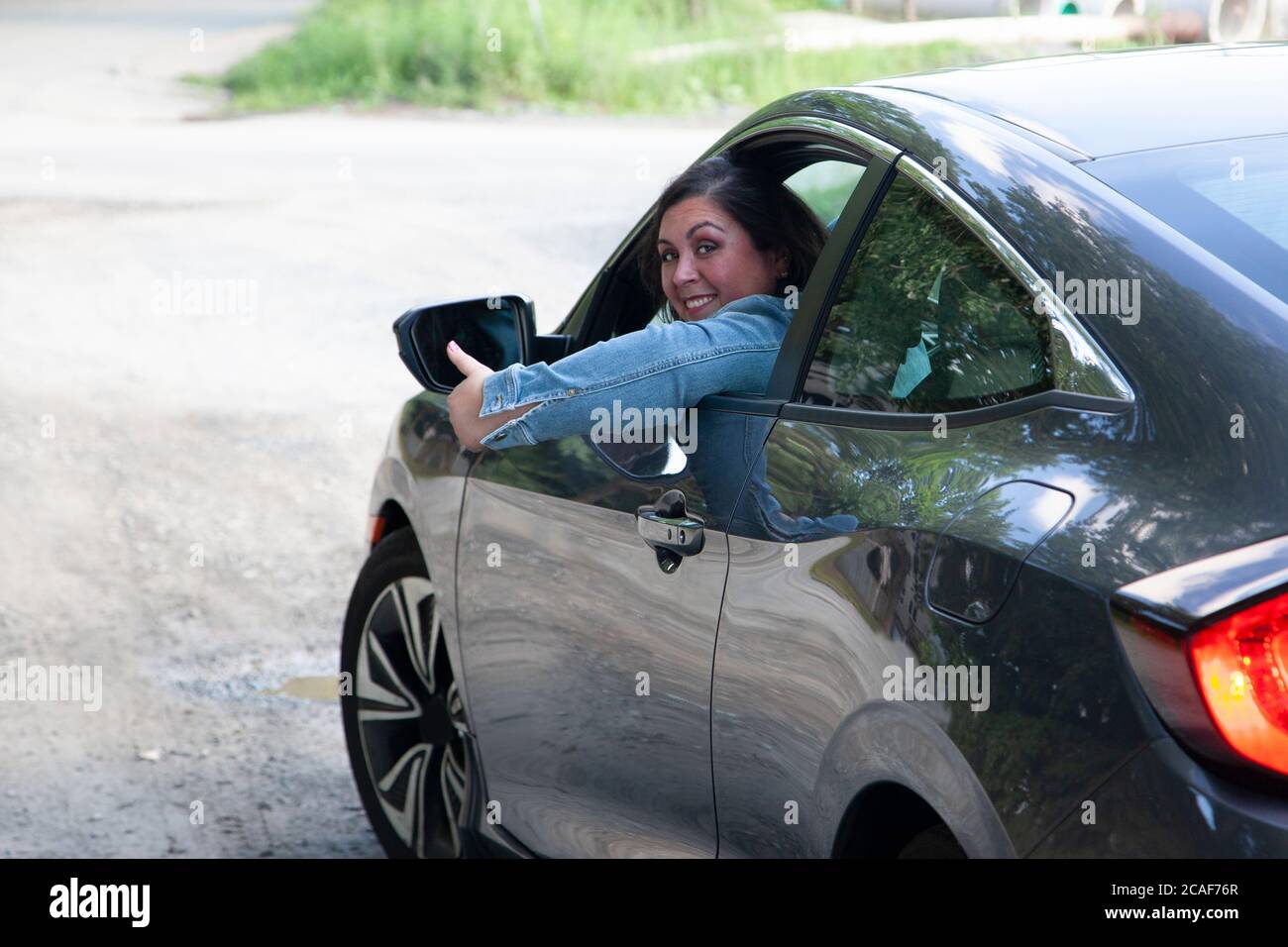 une femme donne un pouce vers le haut comme elle prend sa voiture et quitte la ville Banque D'Images