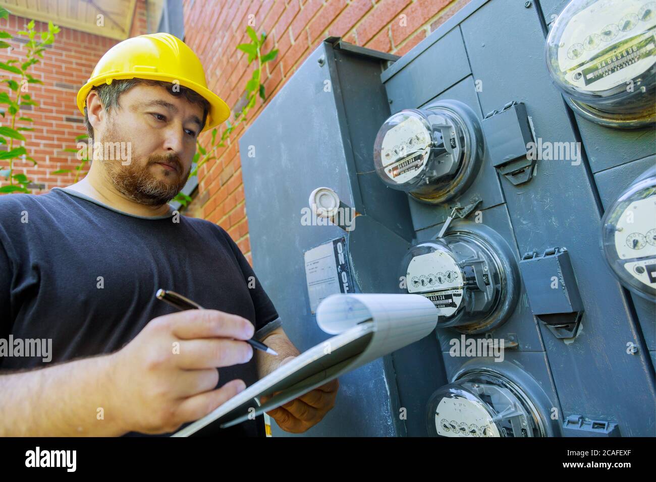 Pendant la vérification, un technicien en casque jaune examine la lecture du compteur sur le presse-papiers Banque D'Images