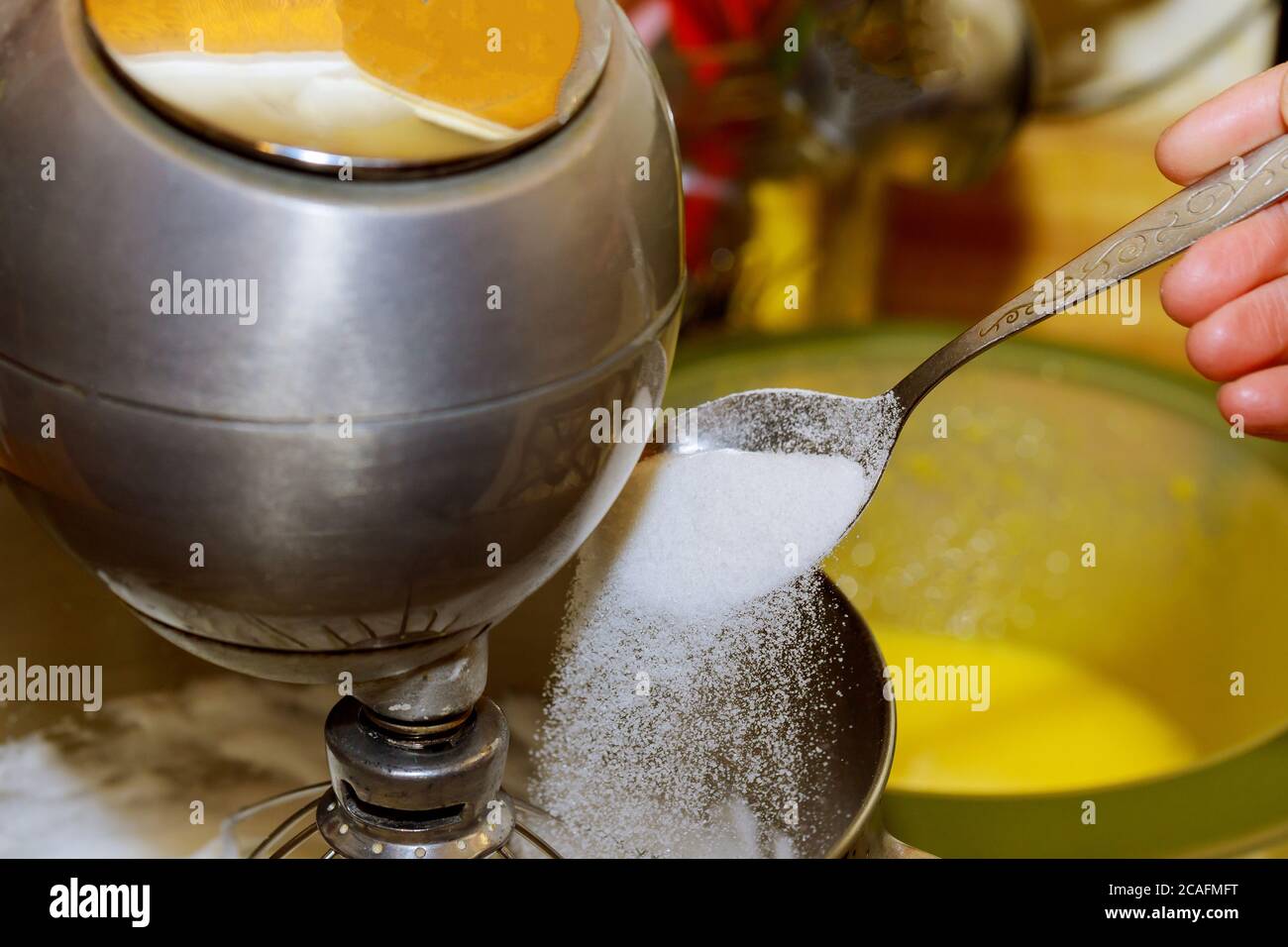 Les mains des femmes ajoutent un sucre dans le bol du batteur avec des blancs d'œufs en fouetter pour faire un gâteau. Banque D'Images