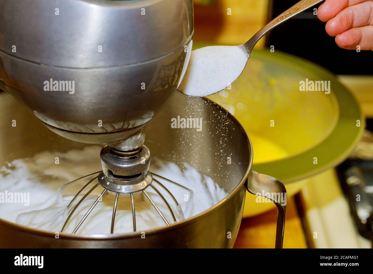 Le batteur fouetter les blancs d'œufs pour le gâteau. La femme ajoute du sucre dans le bol du batteur. Banque D'Images