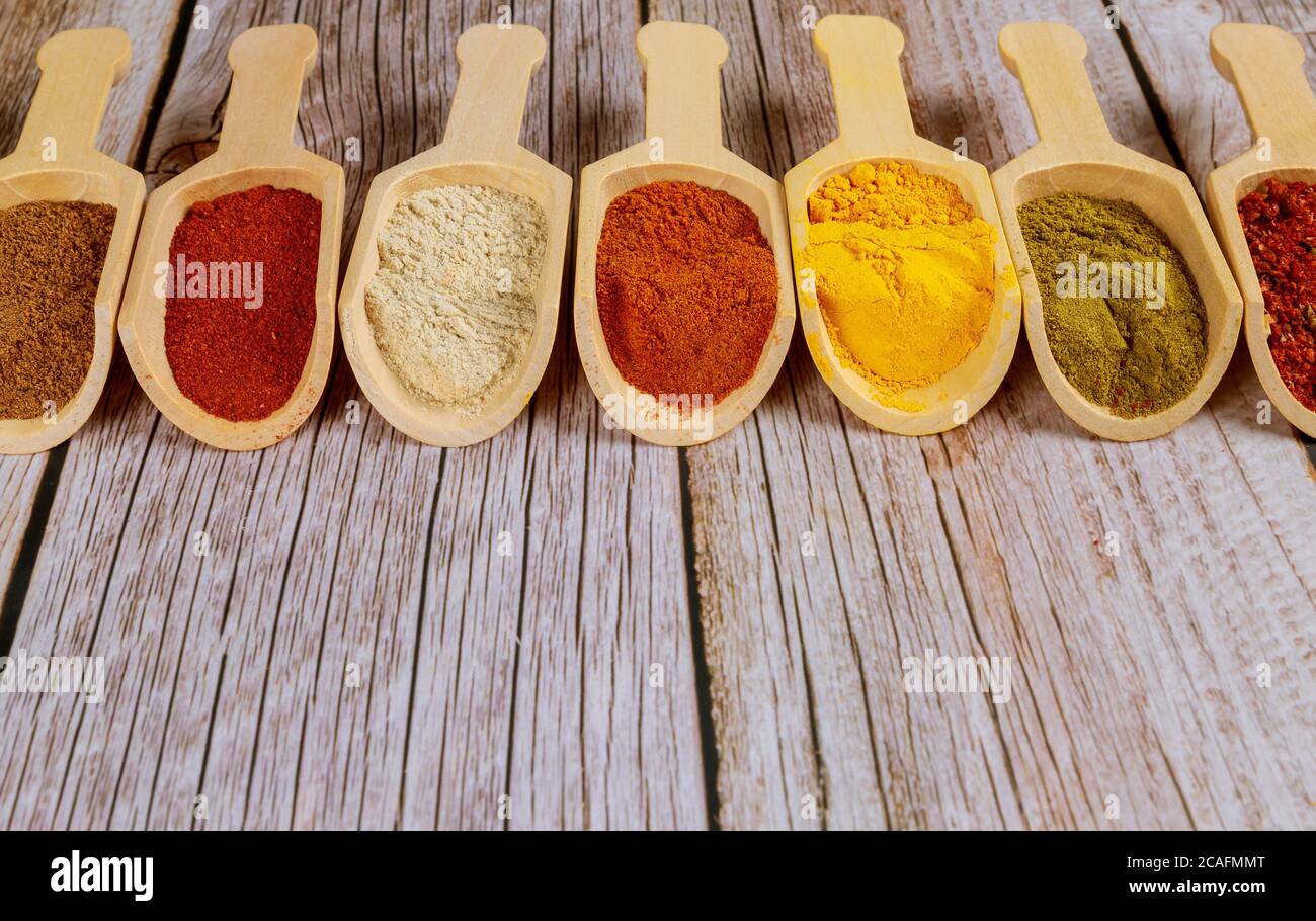 Poudres d'épices moulues colorées en cuillères en bois sur fond blanc en bois. Banque D'Images