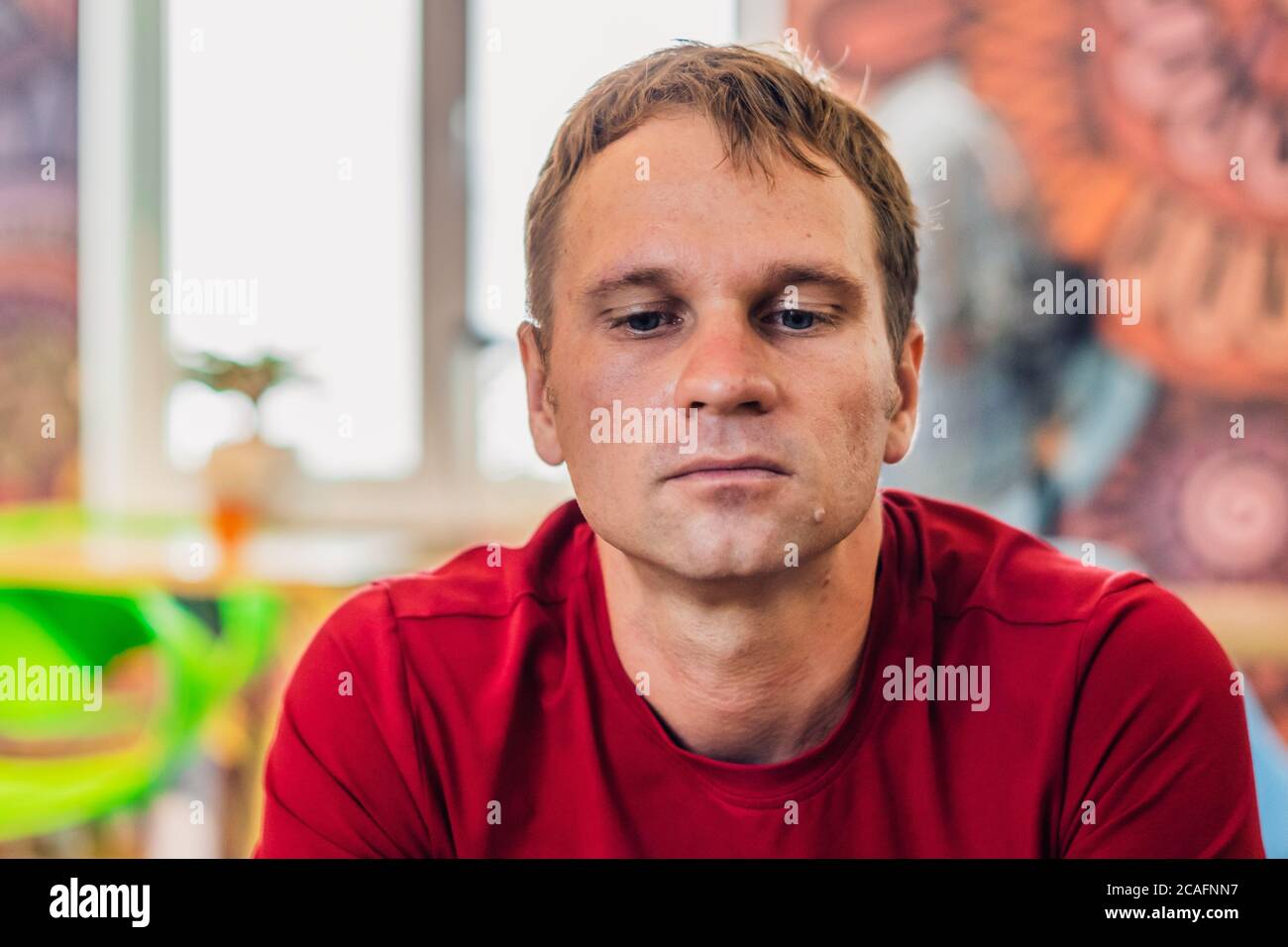 Sérieux triste beau homme blond dans un style décontracté t-shirt rouge s'asseoir regarder, en attendant quelqu'un ou des changements, penser. Peau sans photoshop. Relation humaine Banque D'Images