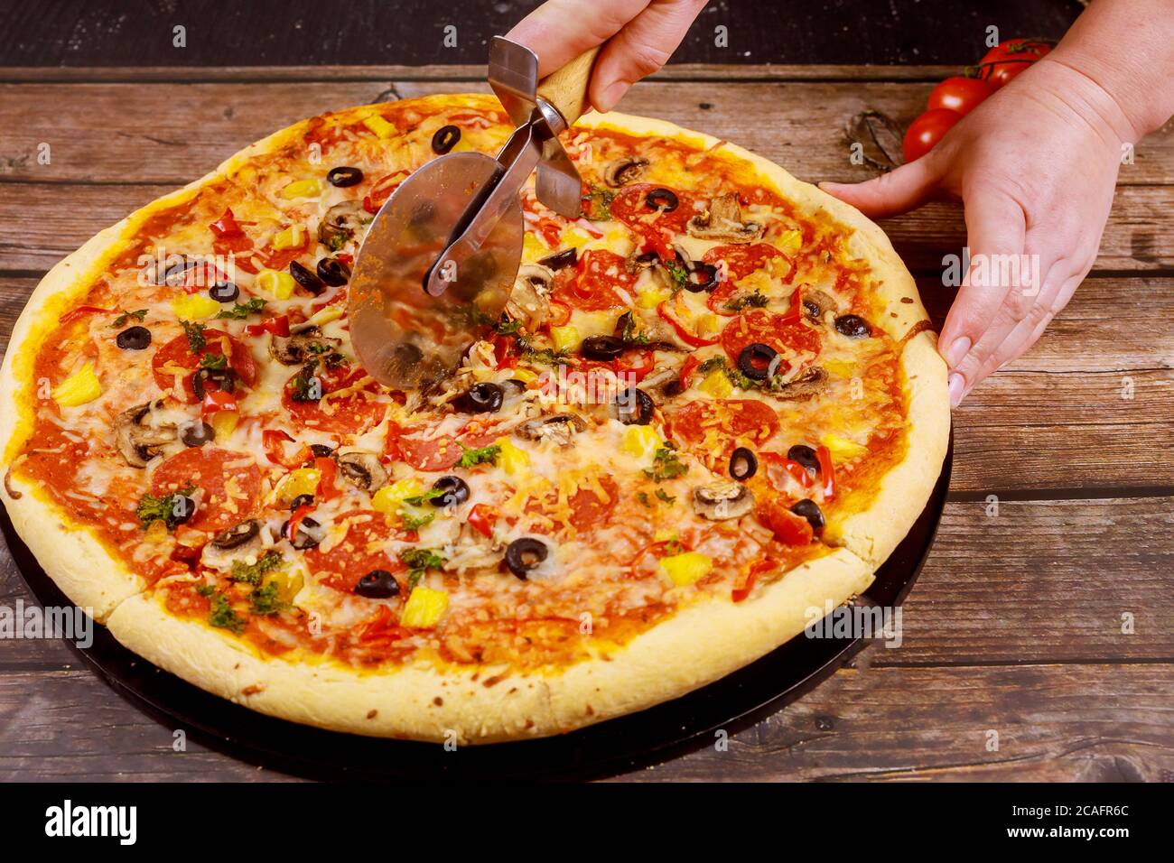 Le chef a coupé une pizza suprême avec un couteau sur fond de bois. Banque D'Images